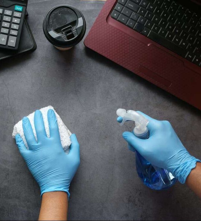 Cleaning desktop with detergent in spray and hand in blue gloves